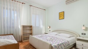 Ein Schlafzimmer mit einem Bett, einem Nachttisch, einer Wand-Klimaanlage und einem Fenster mit durchsichtigen Vorhängen.