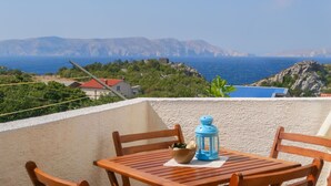 Un balcon avec une table, des chaises, une lanterne et une vue sur la mer et les montagnes.