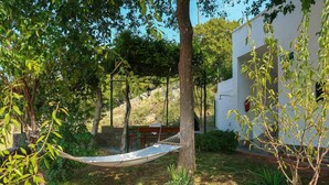 Un hamac dans un espace jardin, avec un bâtiment blanc en arrière-plan.