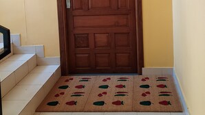 A wooden door with a handle and a keyhole, a small light fixture above it, and a doormat with fruit patterns at the entrance. - Studio Apartment Suite with kitchenette (THIRUVANANTHAPURAM)