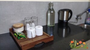 A kitchen counter with a wooden tray holding salt, pepper shakers, a glass bottle, and a coffee maker. - Studio Apartment Suite with kitchenette (THIRUVANANTHAPURAM)