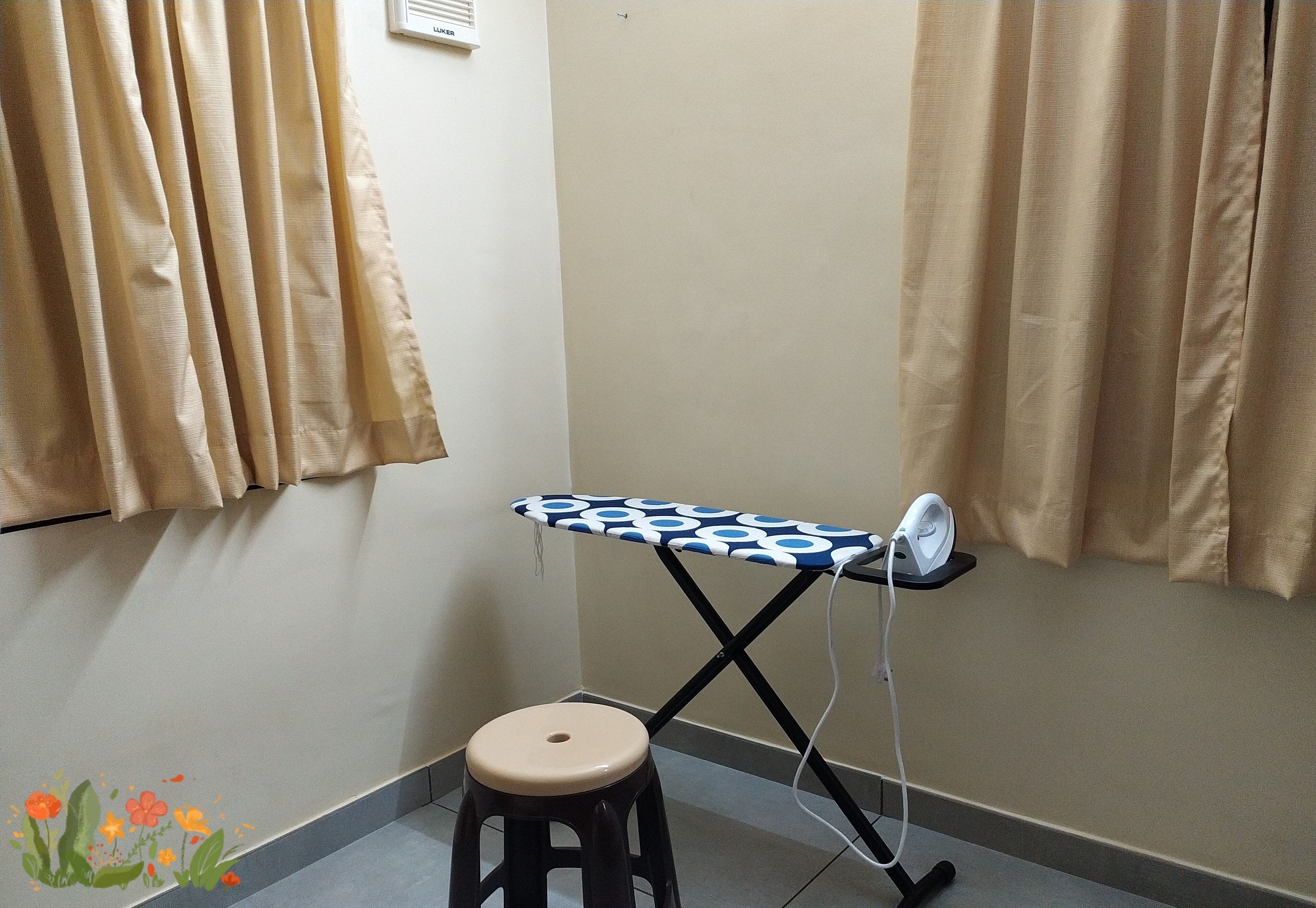 Une chambre d’angle équipée d’une planche à repasser, d’un tabouret, de rideaux beiges et d’un climatiseur fixé au mur.