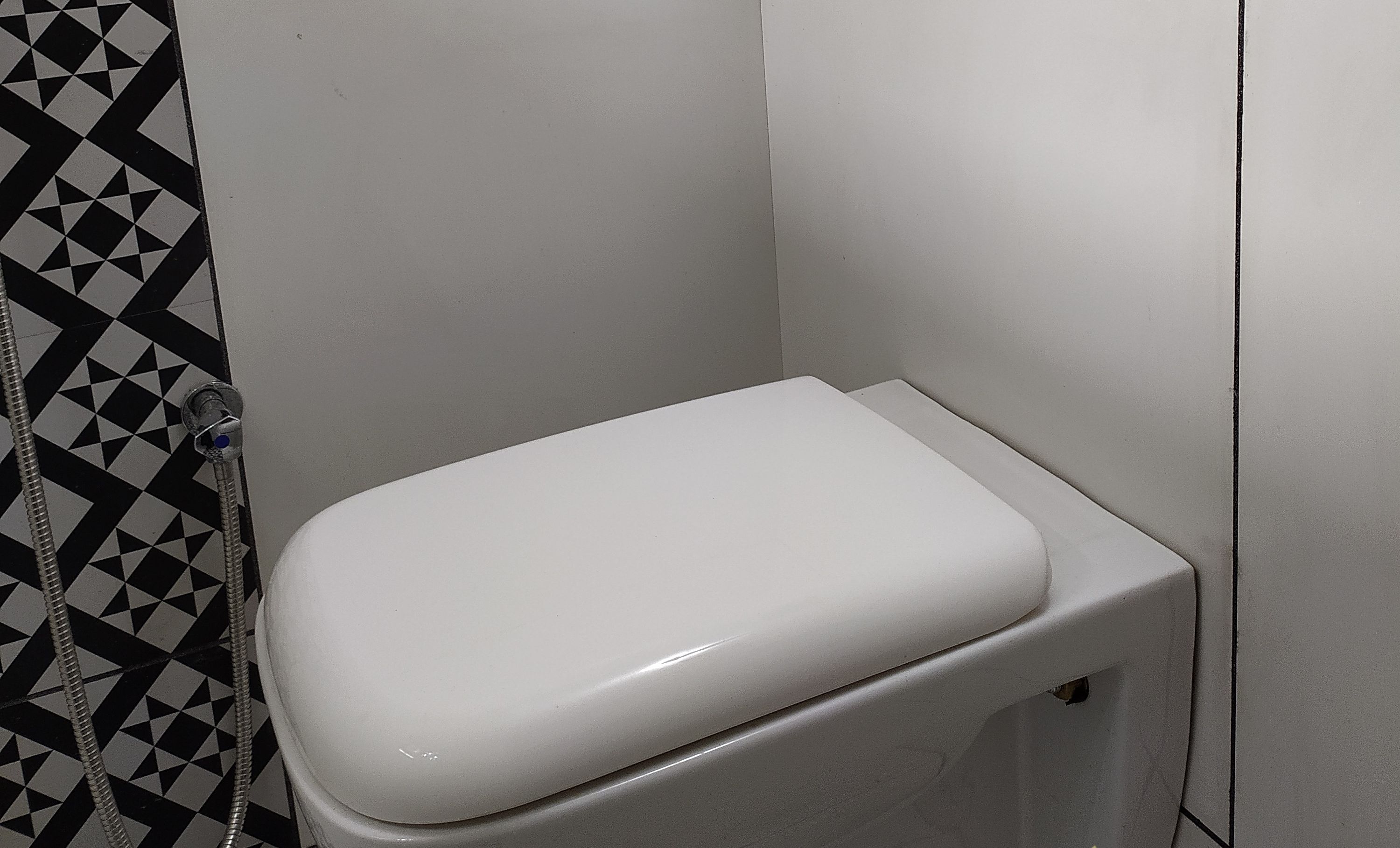 Un inodoro con asiento y tanque blancos, pared con diseño blanco y negro y una manguera de agua.