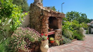 Een buitenkeuken van natuursteen met een schoorsteen, omringd door planten en bloemen in potten.