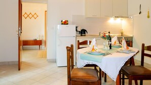 Een eethoek met een tafel voor twee personen, een koelkast en een keuken op de achtergrond.