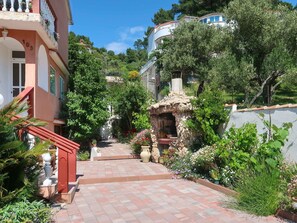 Stroll through a serene garden, surrounded by lush greenery and vibrant flowers, to a charming structure with a balcony and red staircase.