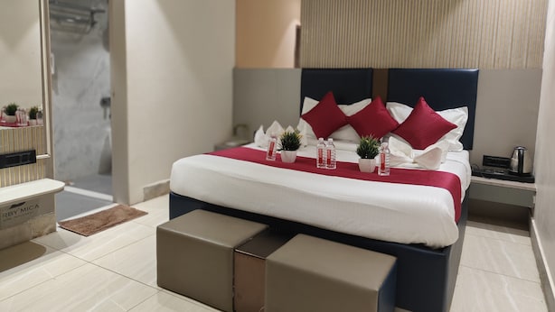 A modern hotel room with a neatly made bed, a bedside table, a nightstand, and a small potted plant. - Hotel Shirdi Park Inn 80 Meters From Sai Samadhi Temple (Rahata)