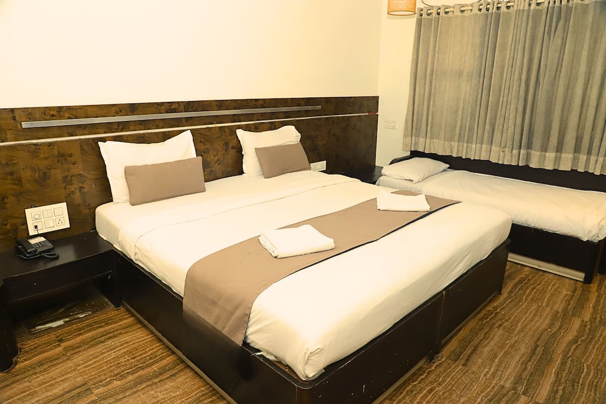 A hotel room with a large bed, a smaller bed, a nightstand with a phone, and a window with curtains.