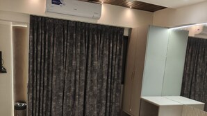 A modern hotel room with a large bed, a ceiling fan, an air conditioning unit, a bathroom with a mirror, and a red rug. - Hotel Shirdi Park Inn 80 Meters From Sai Samadhi Temple (Rahata)