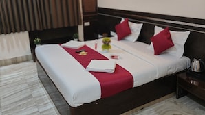 A hotel room with a large bed, a nightstand, a ceiling fan, a wall-mounted light, and a painting. - Hotel Shirdi Park Inn 80 Meters From Sai Samadhi Temple (Rahata)