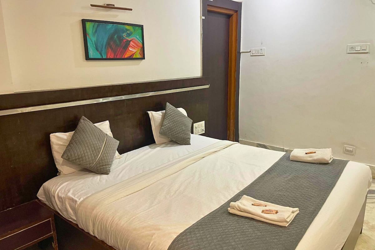 A neatly made bed with white linens and gray pillows, a gray quilted blanket, and a folded towel on the bed.