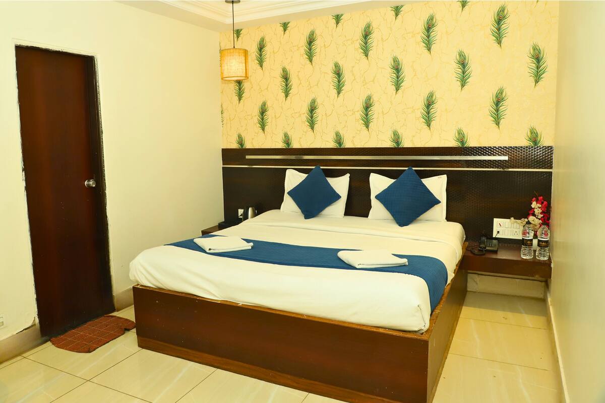 A neatly made bed with blue and white bedding, a wooden headboard, and a wall with a leaf pattern.