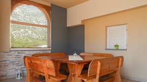 Una mesa de madera con bancos en una habitación con paredes de piedra, un ventanal grande y una pequeña planta en maceta.