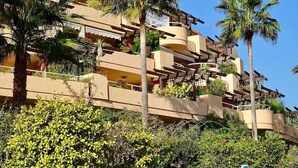 A multi-story hotel with balconies, palm trees, and a clear blue sky.