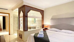 A hotel room with a large bed, a bathroom with a mirror, and a view of the bathroom through a partition.