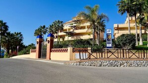 A gated entrance with a blue roof, palm trees, and a multi-story building with balconies.