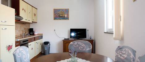 A compact living space with a dining table, chairs, a television, and a kitchen area.