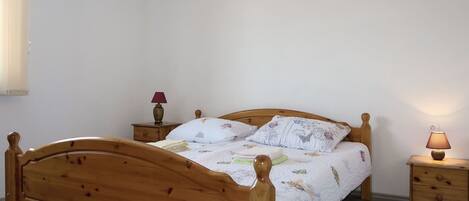 Una cama de madera con una colcha floral, dos mesitas de noche con lámparas y una ventana con cortinas.