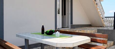 Une table avec une bouteille et un saladier de fruits, un banc en bois et un sol carrelé en pierre.