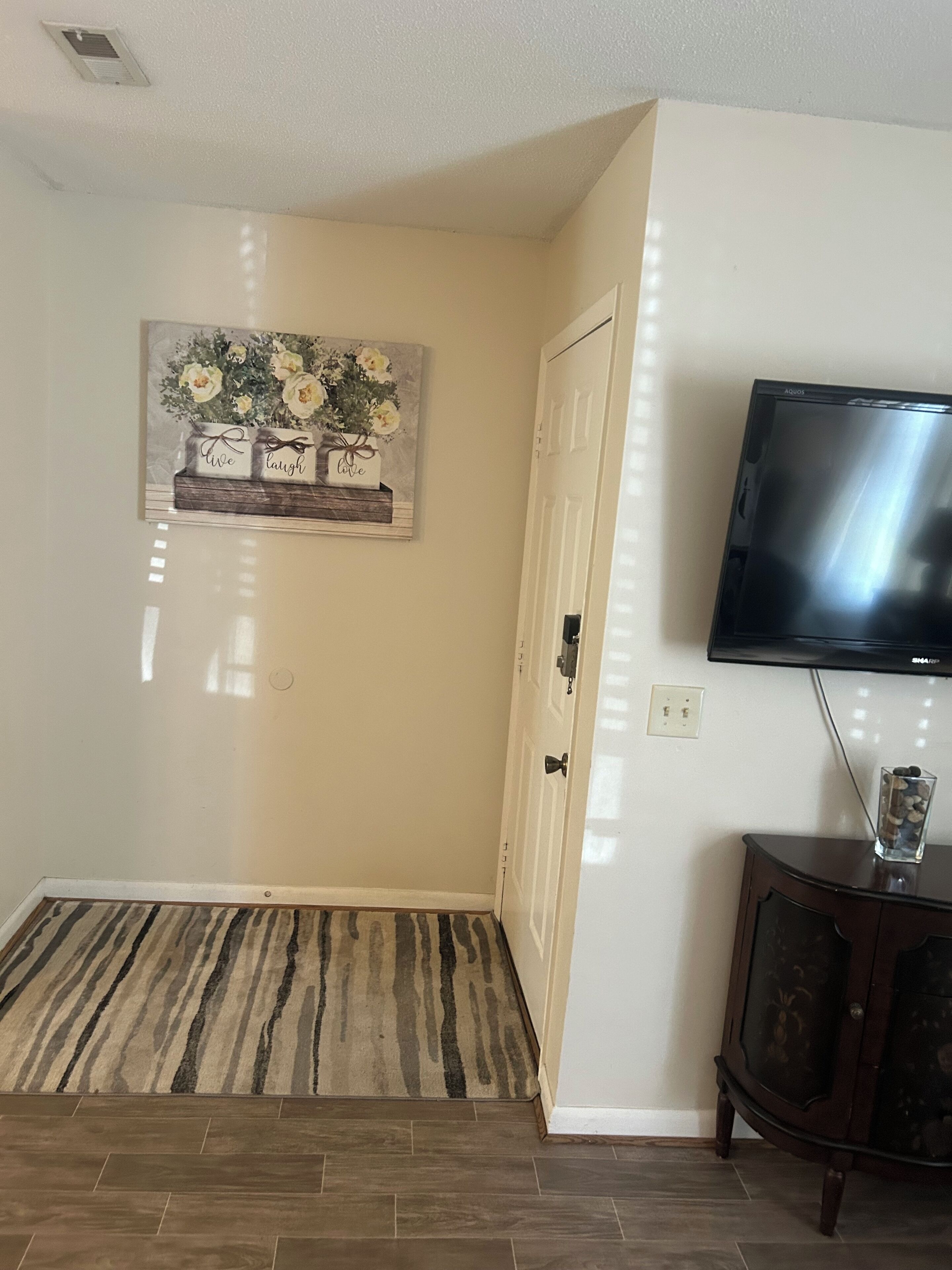 Ein Zimmer mit Holzboden, einem Blumenbild, einem Fernseher und einem Schrank.