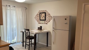 Una cocina compacta con una mesa, sillas, refrigerador y un cubo de basura.
