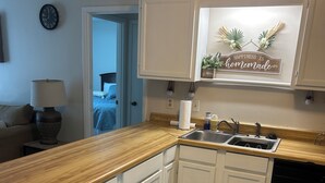 Una cocina con armarios blancos, encimera de madera, fregadero y lavavajillas.