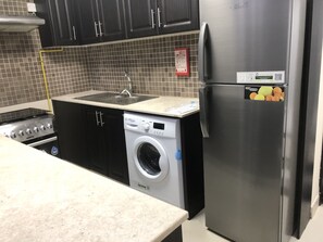A kitchen with a stainless steel refrigerator, a washing machine, a stove, and a sink.