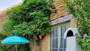 Un patio con mobiliario exterior, un muro de piedra y una pequeña zona de jardín con flores.