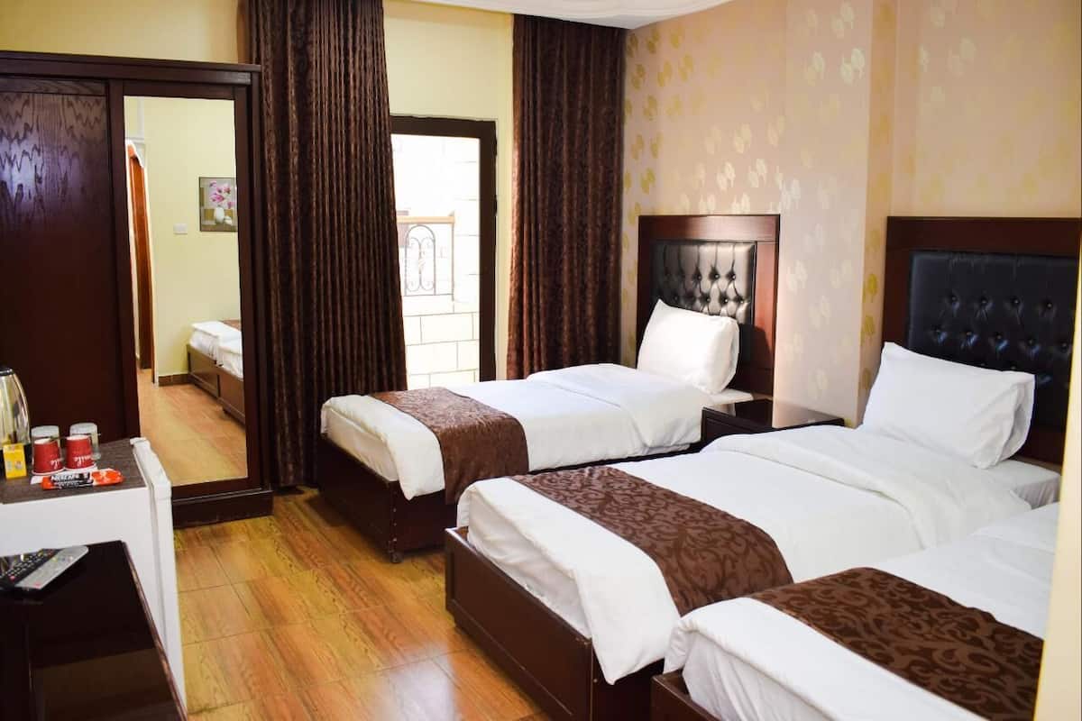 Habitación de hotel con tres camas, un escritorio con teléfono y cafetera, y un espejo que refleja la habitación.