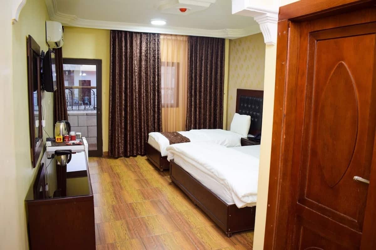 Una habitación de hotel con piso de madera, dos camas, un escritorio con hervidor y un espejo.