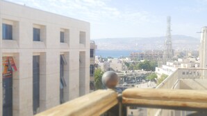 Vista da un balcone su una città con edifici e una lontana visuale del mare.