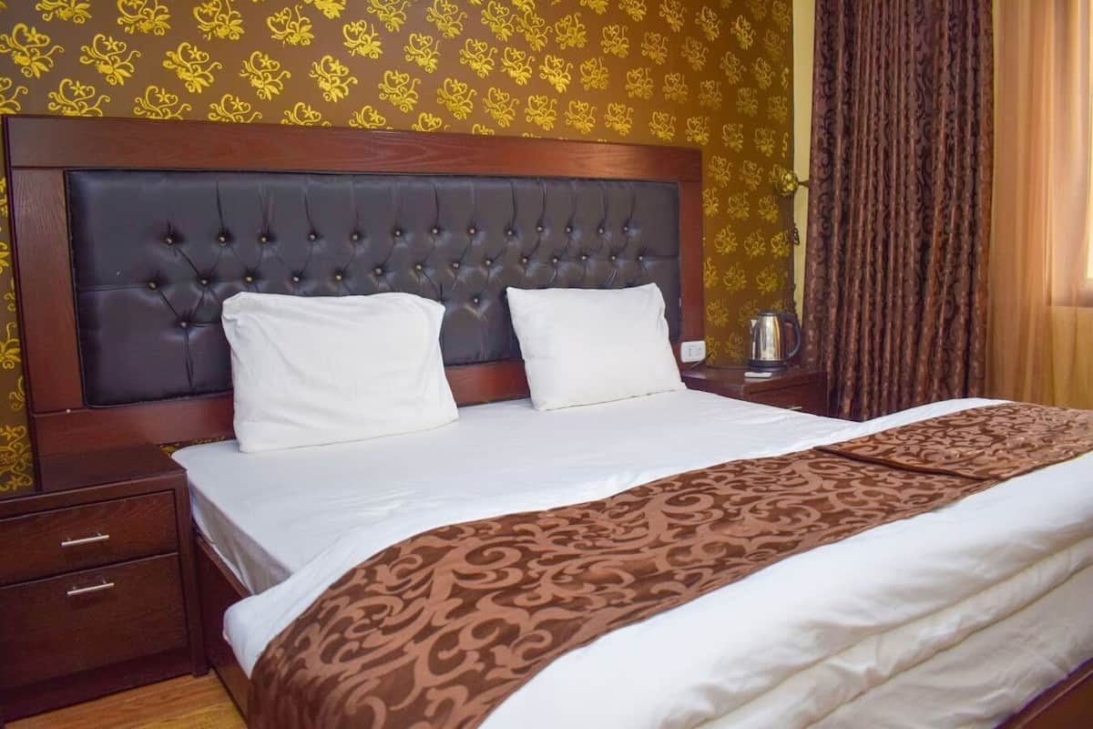 Una habitación de hotel con una cama grande, cabecera de madera y papel tapiz estampado.