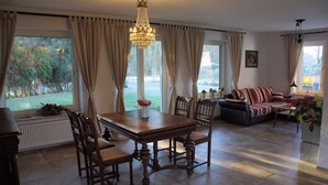 Un salon spacieux avec un coin repas, de grandes fenêtres et un lustre.