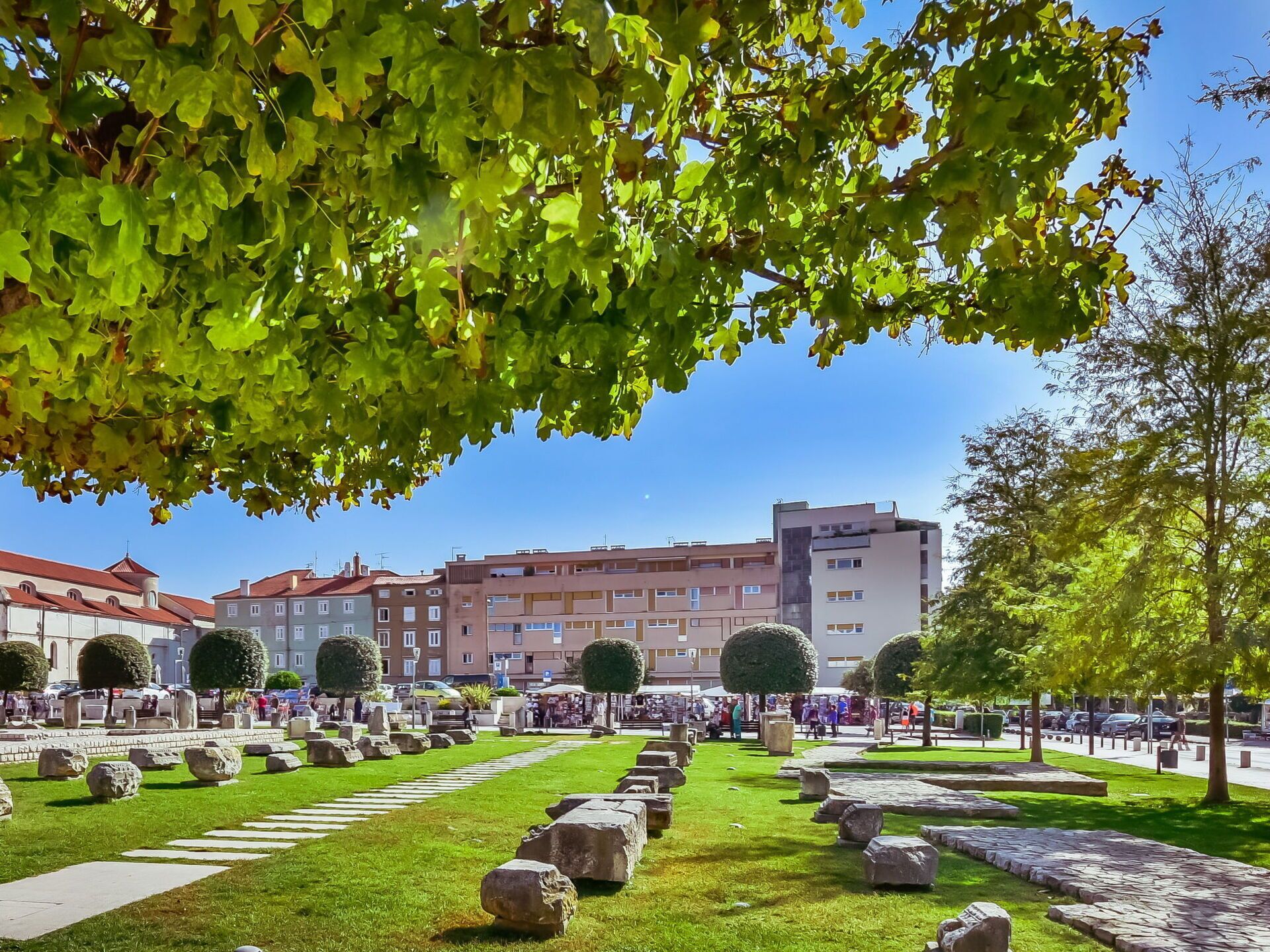 A public square with stone benches, a clear sky, and buildings in the background.