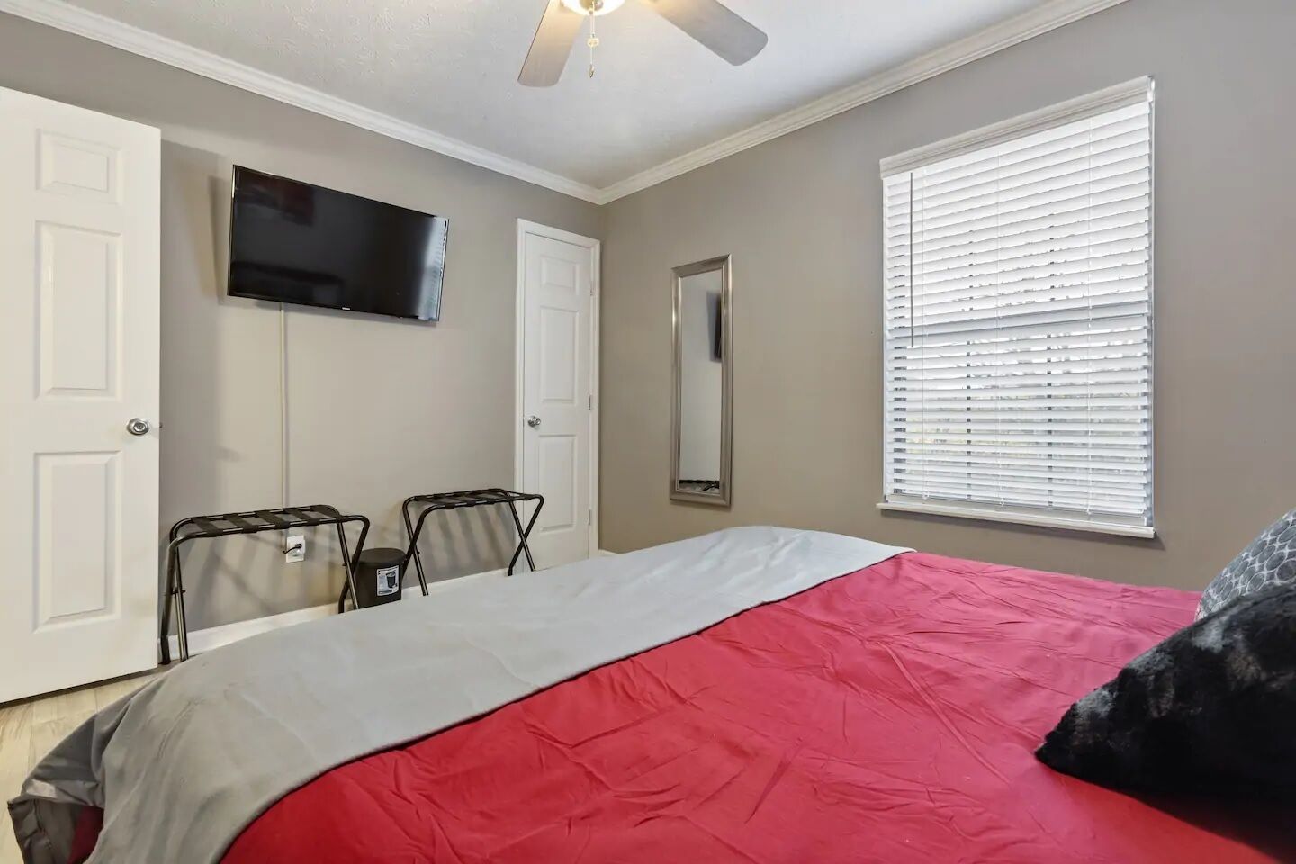 Quarto com cama, ventilador de teto, TV montada na parede e janela com persianas.