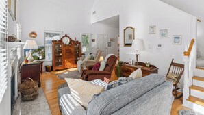 A spacious living room with a high ceiling, a wooden staircase, and a view of the outdoors through a window. - Little Gingerbread Cabin Two Bedroom Two Bath Home with Rocking Chair Porch (Saint Simons Island)