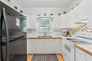 A kitchen with white cabinets, a black refrigerator, a window with blinds, and a stove.