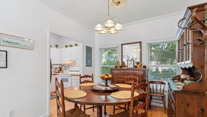 A dining room with a wooden table, chairs, and a chandelier. - Little Gingerbread Cabin Two Bedroom Two Bath Home with Rocking Chair Porch (Saint Simons Island)