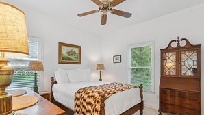 A bedroom with a bed, a wooden dresser, a ceiling fan, and two windows with blinds. - Little Gingerbread Cabin Two Bedroom Two Bath Home with Rocking Chair Porch (Saint Simons Island)