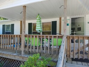 Una terraza de madera con un paraguas a rayas verdes, una silla verde y una mesa.