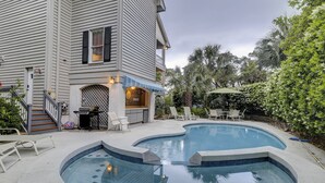 Ein zweistöckiges Haus mit Garten, Swimmingpool, Grillplatz und einer Terrasse mit Stühlen.
