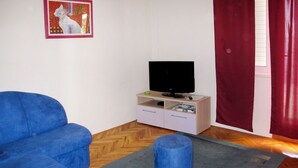 Een woonkamer met een blauwe bank, een televisie op een houten kast en een rood gordijn.