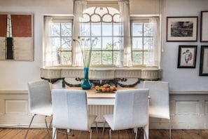 Un comedor con una mesa lista para dos comensales, un florero con flores y una ventana con cortinas.