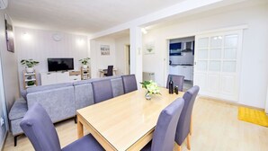 Un comedor moderno con una mesa de madera y sillas a juego, un televisor y una cocina visible a través de una puerta abierta.
