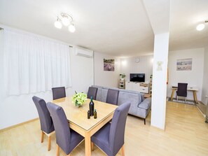 Una sala de estar moderna con comedor, un sofá gris, un televisor y un escritorio pequeño.