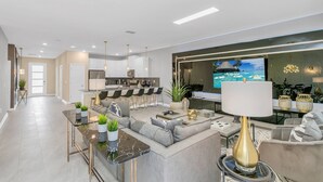 Una sala de estar moderna con un sofá, una mesa de centro y un televisor. Se observa una cocina al fondo con taburetes de bar.
