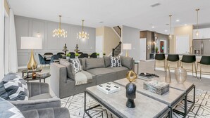 Una sala de estar moderna con un sofá gris, una mesa de centro y un comedor con candelabro.