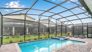 Una piscina con cerramiento de vidrio, rodeada por un patio con sillones de descanso.