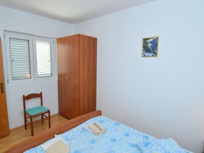 Une chambre à coucher avec un lit, une armoire en bois, une chaise et une fenêtre avec des stores.