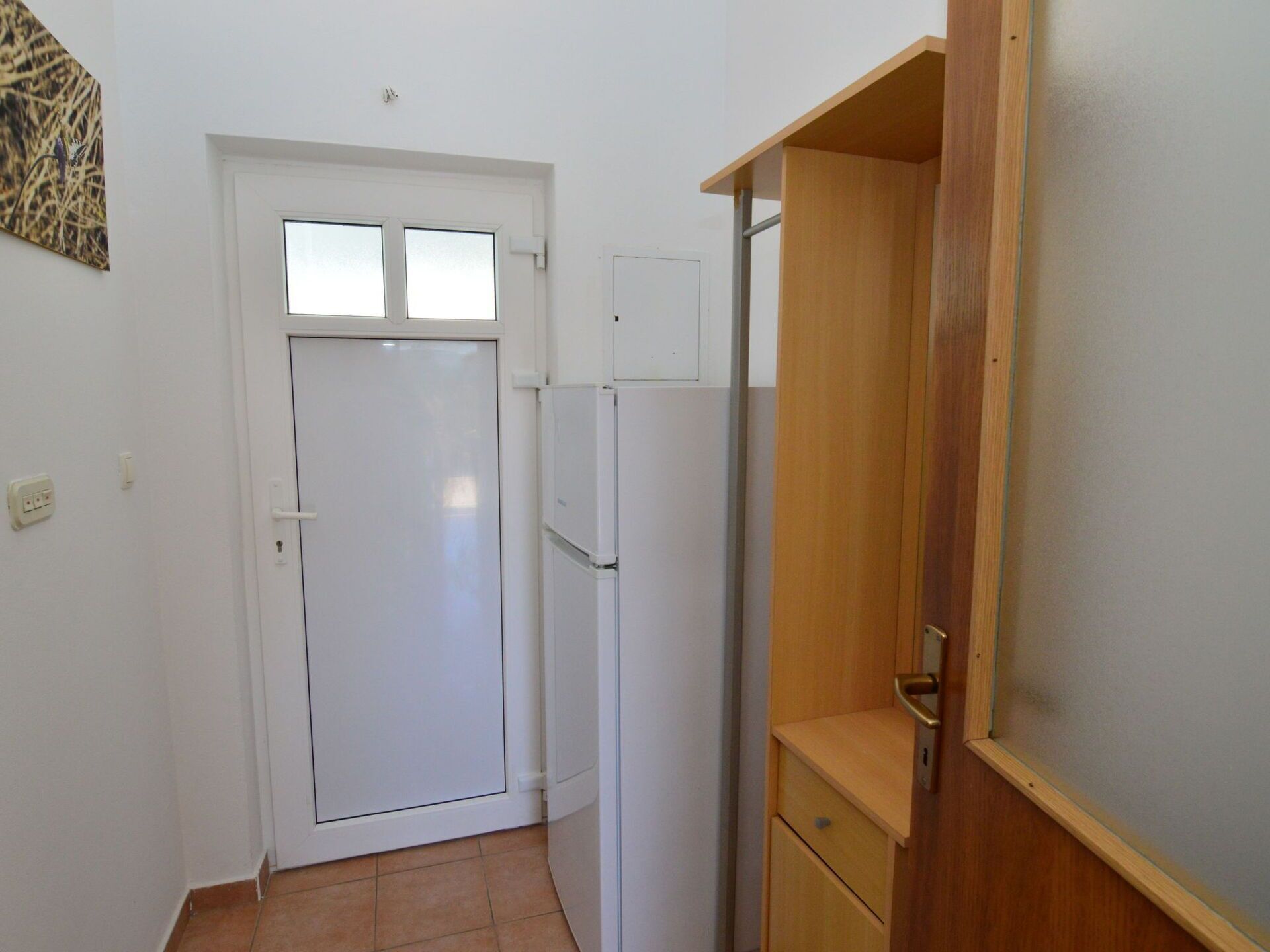 Un couloir étroit avec une porte blanche, un réfrigérateur blanc et un meuble en bois.